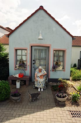 eine ältere Frau sitzt vor ihrem Haus und füttert eine Katze