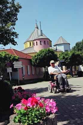 ein Mann im Rollstuhl, im Hintergrund die Dorf-Kirche