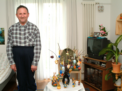 ein Mann steht in seinem Zimmer, rechts daneben ein Tisch mit Osterdekoration