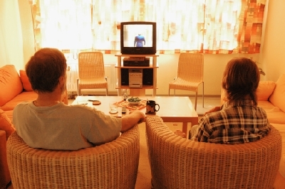 zwei Männer sitzen in Korbstühlen vor dem Fernseher