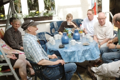 ältere und jüngere Personen sitzen auf der Terrasse und trinken Kaffee