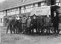 Ein Gruppenbild mit Männern vor einem Anhänger und einem Gebäude