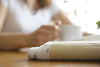 eine Zeitung liegt auf dem Tisch, im Hintergrund hält eine jüngere Frau eine Tasse in der Hand