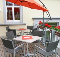 Blick auf die Terrasse mit Tischen und Stühlen und einem Sonnenschirm.